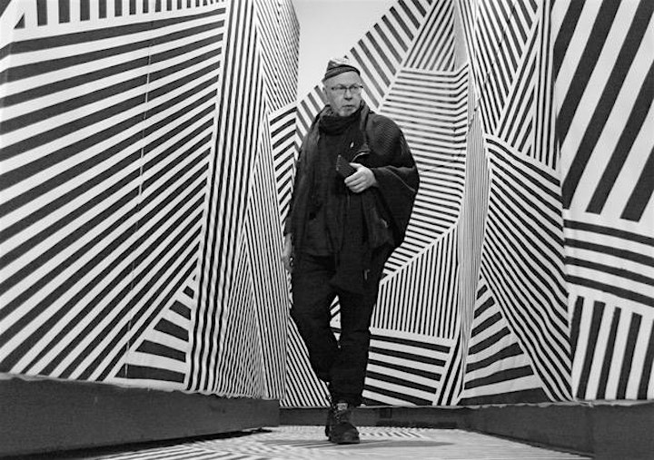  A black and white portrait of artist Ernest Daetwyler in motion walking through a striped hallway.