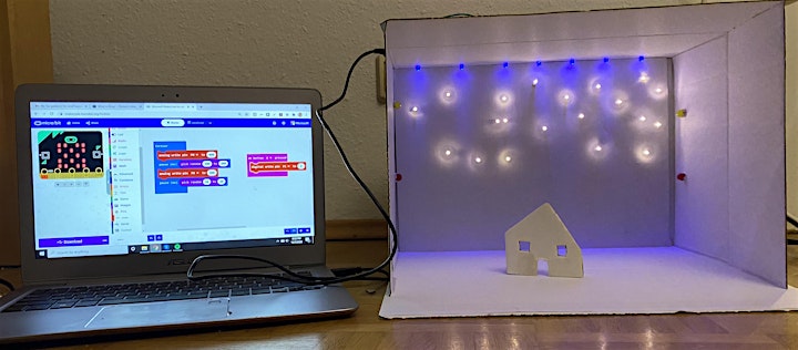 A laptop displaying the microbit software attached to a card box full of blue and white lights and a simple cardboard house.